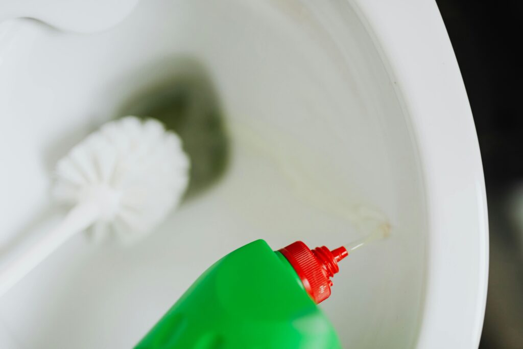 Envase verde de limpieza junto a un inodoro y un cepillo blanco